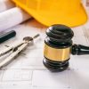 Construction and Labor law. Judge gavel and design tools on building blueprint, close up Construction and Labor law. Yellow safety helmet and judge gavel on building blueprint plans, close up view.